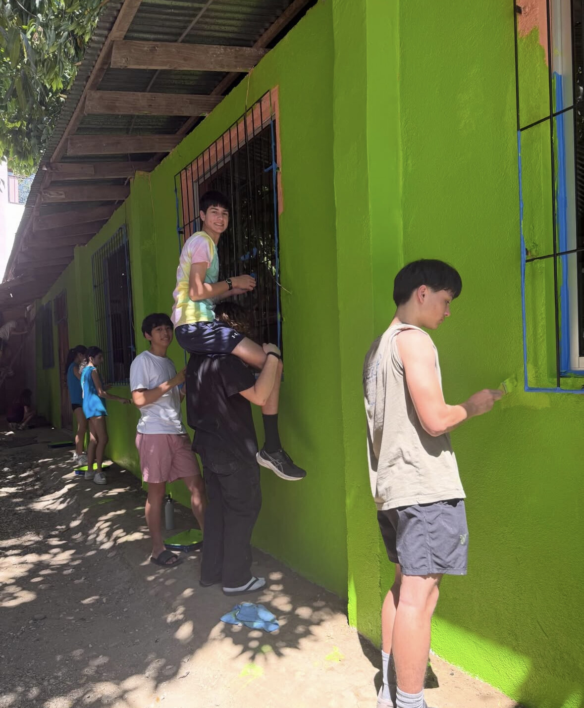 Students helping each other paint a high window at the church